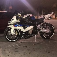 a white and blue motorcycle parked next to a red car in a parking lot at night