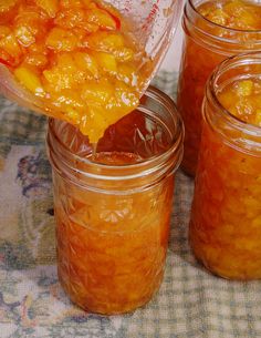 a person pouring orange sauce into jars on a table