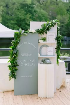 an outdoor ceremony setup with greenery and white flowers on the back of a sign