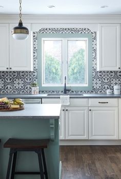 a kitchen with white cabinets and an island in front of a window that looks out onto the woods