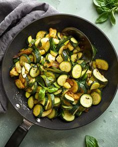 a pan filled with zucchini and other vegetables on top of a blue surface