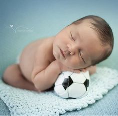 a baby laying on top of a blanket with a soccer ball in it's mouth