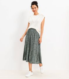 a woman standing in front of a white wall wearing a green pleaed midi skirt