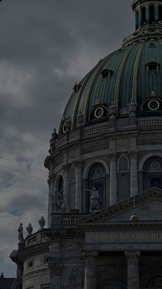 an old building with a green dome on top under a cloudy sky and some power lines