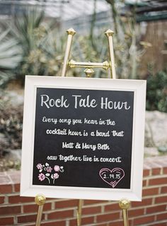 a sign with writing on it in front of a brick wall and potted plants