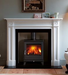 a wood burning stove in a living room next to a white chair and painting on the wall