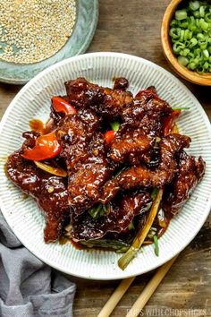 a white plate topped with meat covered in sauce and vegetables next to chopsticks