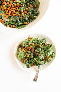 two bowls filled with greens and chickpeas on top of a white tablecloth