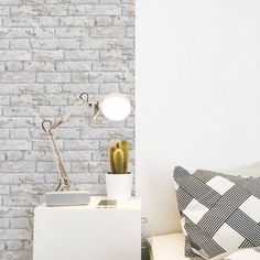 a white brick wall next to a bed with pillows and a lamp on top of it