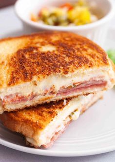 a sandwich cut in half sitting on top of a white plate next to a bowl of salad