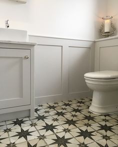 a white toilet sitting next to a sink in a bathroom under a window on top of a tiled floor