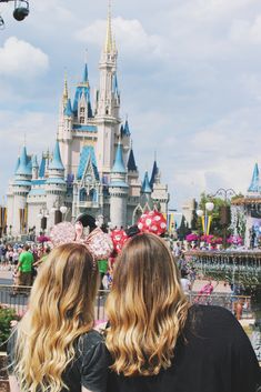 two women standing in front of a castle at disney world with their backs to the camera