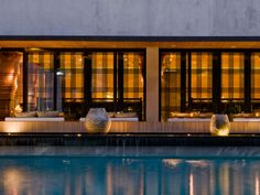 an outdoor swimming pool next to a large building with glass doors and windows at night