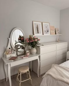 a bedroom with white furniture and flowers in vases on the dresser next to it