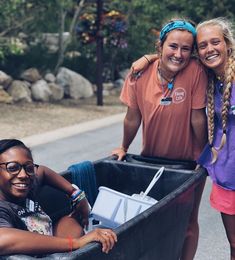 three girls are in the back of a dumpster and one girl is holding a cooler