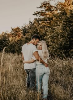 a man and woman are standing in the tall grass with their arms around each other