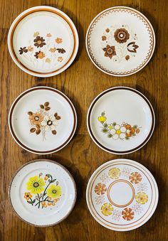 four plates with flowers painted on them sitting on a wooden table next to each other