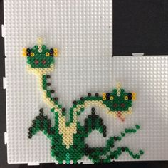 a green and yellow beaded lizard sitting on top of a white board with black squares