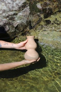 a person laying on the ground next to a body of water with a vase in it