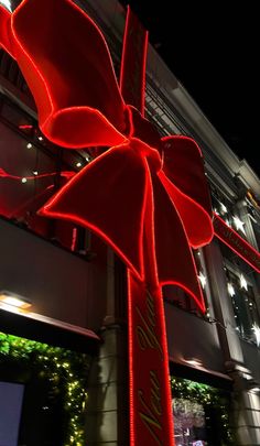 a large red bow on the side of a tall building at night with lights in the background