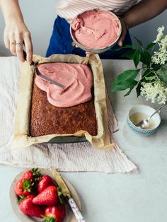 a woman is spreading frosting onto a cake with strawberries on the plate next to it