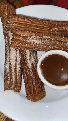 some churros are on a white plate with chocolate sauce in the middle and powdered sugar on top