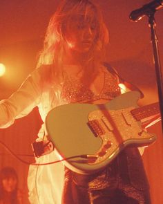 a woman holding an electric guitar while standing in front of a microphone