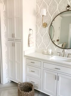 a bathroom with white cabinets and a large mirror on the wall above the sink, along with a wicker basket in front of it