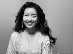 a black and white photo of a smiling woman with wine glasses in front of her