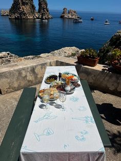 a table that has some food on it near the water and boats in the background