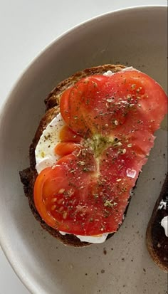 an open face sandwich with tomatoes and cream cheese on it in a white bowl sitting on a table