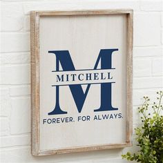 a wooden sign hanging on the side of a white brick wall next to a potted plant