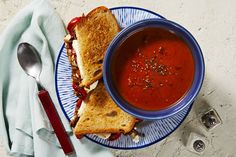 a bowl of soup and a sandwich on a blue plate with a spoon next to it