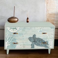 a blue and white chest with a turtle painted on the side, next to a vase