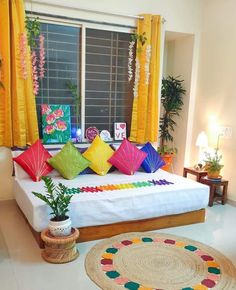 a bed with colorful pillows on top of it in front of yellow curtains and potted plants