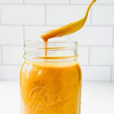 a glass jar filled with orange liquid on top of a white counter next to a knife