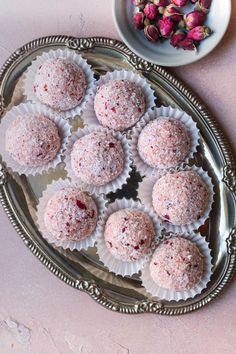 a platter filled with pink sprinkled donuts next to a bowl of rose buds