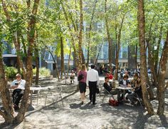 people are sitting at tables in the middle of a park with trees and benches around them