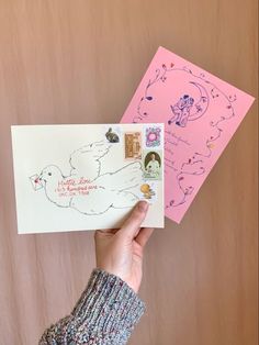 a person holding up two greeting cards in front of a pink envelope with an image of a dove on it