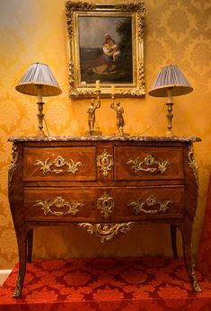 an antique dresser with two lamps and a painting on the wall