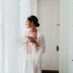 a woman standing in front of a window wearing a white robe and feathered shawl