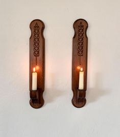 two wooden wall sconces with lit candles on each one, against a white wall