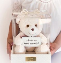 a person holding a white teddy bear in a clear box with writing on the front