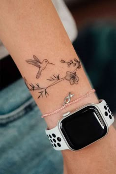 a woman's arm with a bird and flower tattoo on the left side of her wrist