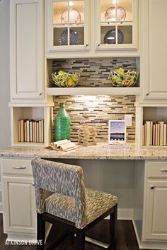 a home office with white cabinets and marble counter tops, along with a green vase on the desk