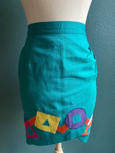 Vintage Skirt in Bright Teal Green with multi color geometric graphic shapes appliquéd on  -skirt is tulip shaped  -zips and buttons in the back  -waist has elastic in part of band  -Made by Deborah Lunt Boutique  Measurements laying flat: waist 12.5 inches / stretched 14 inches  Length 22.5" Retro Fitted Skirt With Pockets, Retro Fitted Pencil Skirt For Spring, Retro Fitted Mini Skirt With Pockets, Spring Retro Fitted Pencil Skirt, Retro Fitted Mini Skirt, Fitted Retro Cotton Mini Skirt, Retro Party Mini Skirt With Lined Detail, Maximalist Clothes, Green Fitted Retro Mini Skirt