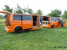 an orange van is parked in the grass with its doors open and people standing next to it