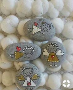 three painted rocks sitting on top of some white balls with hearts and angel figures drawn on them