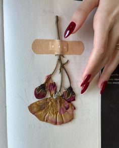 a woman's hand with red nail polish holding a piece of fabric and a flower