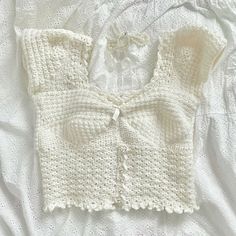 a crocheted sweater with a bow on the front, and a white shirt underneath it